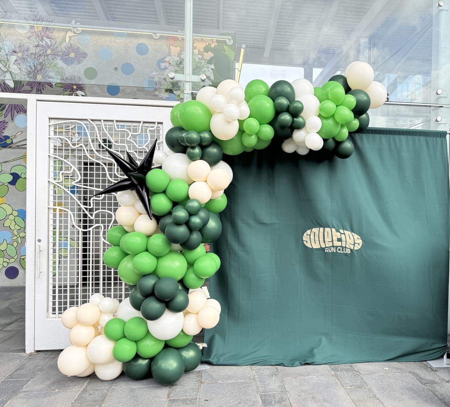 Green and ivory balloon arch with SoleTies Run Club backdrop